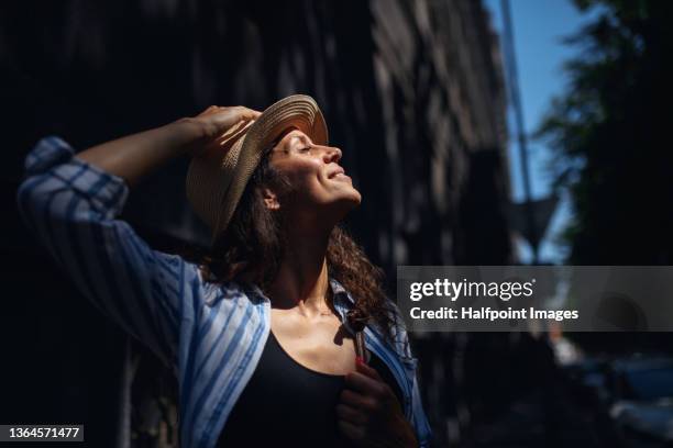 happy young woman with straw hat standing in street with eyes closed in town in summer. - slovakia town stock pictures, royalty-free photos & images