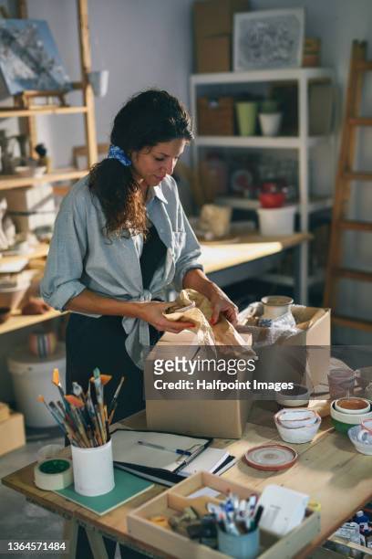 mid adult potter woman, packing her ceramic products to carboard box indoors in art studio, small business concept. - atelier dartiste photos et images de collection