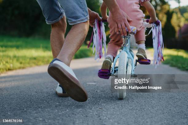 rear view of father teaching his little daughter to ride a bicycle in park, low section. - eventos de la vida fotografías e imágenes de stock