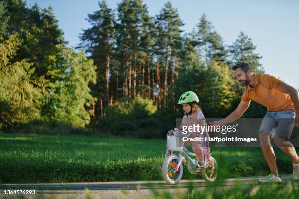 father teaching his little daughter to ride a bicycle in park. - eventos de la vida fotografías e imágenes de stock