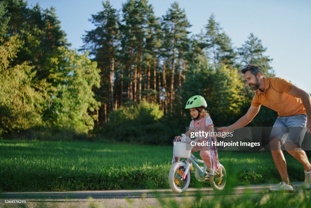 Father teaching his little daughter to ride a bicycle in park.