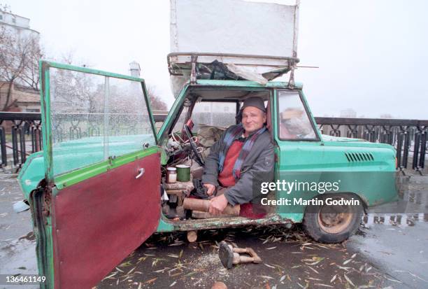 Unknown homeless man who lost legs to a childhood illness, has no inclome and lives in his car, with his belongings on the roof, sawing wood, by the...