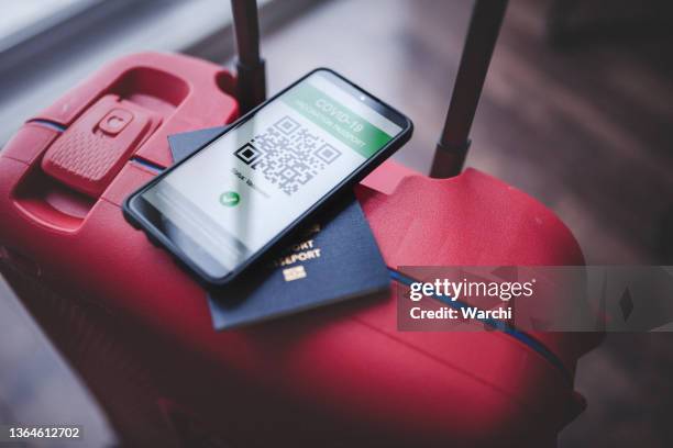 telefon mit covid-19-impfpass und reisepass auf einem roten koffer - impfpass reisedokument stock-fotos und bilder