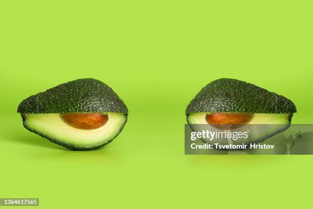 fresh cut avocado shaped like eyes isolated on green background. creative surreal food concept. - avocado isolated stock-fotos und bilder