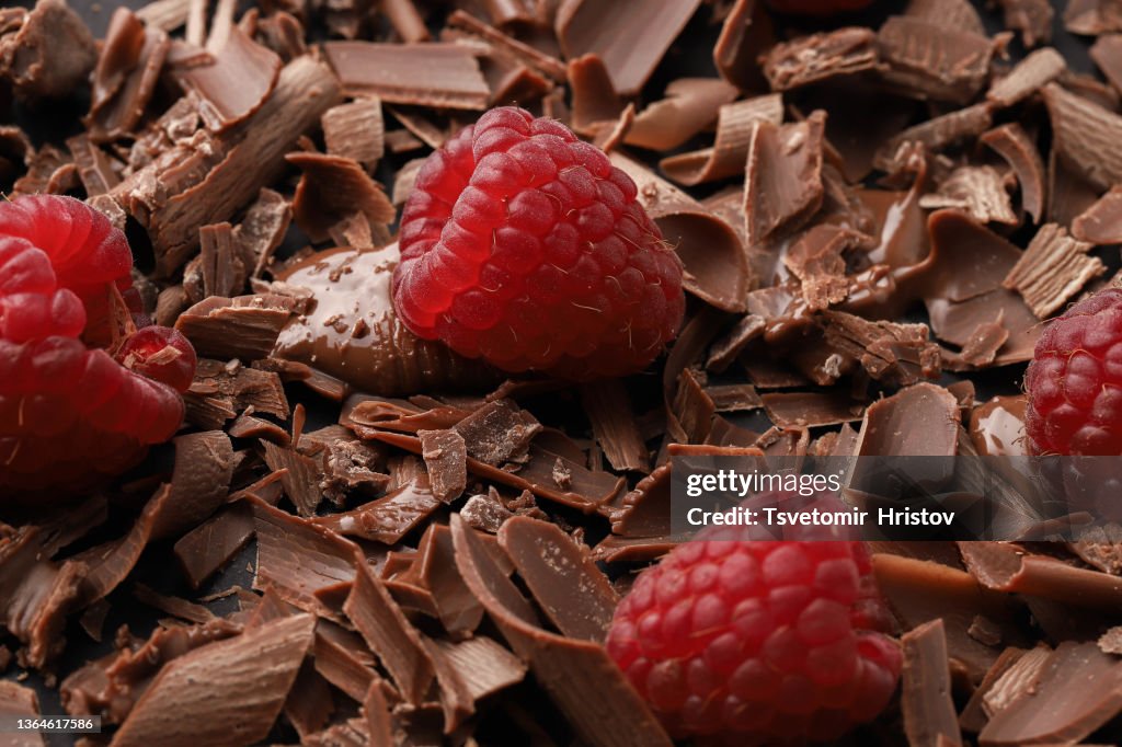 Close-up of chocolate shavings near cocoa beans with fresh raspberries.