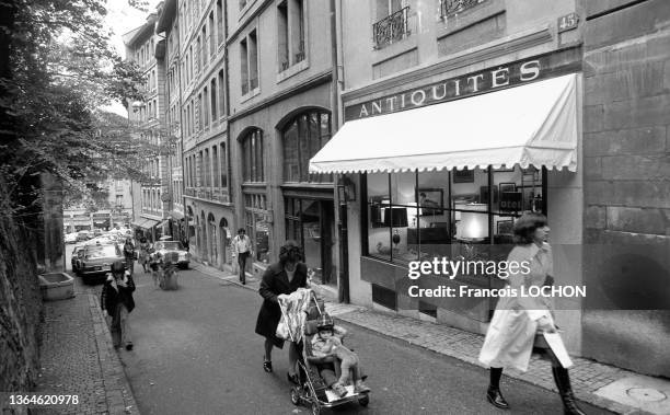 Passants et femme avec une poussette devant une vitrine d'une boutique d'antiquités à Genève en octobre 1975.