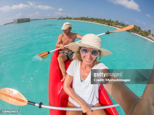 happy young couple taking selfie on red canoe floating over blue lagoon in tropical vacation destination - wide angle stock pictures, royalty-free photos & images