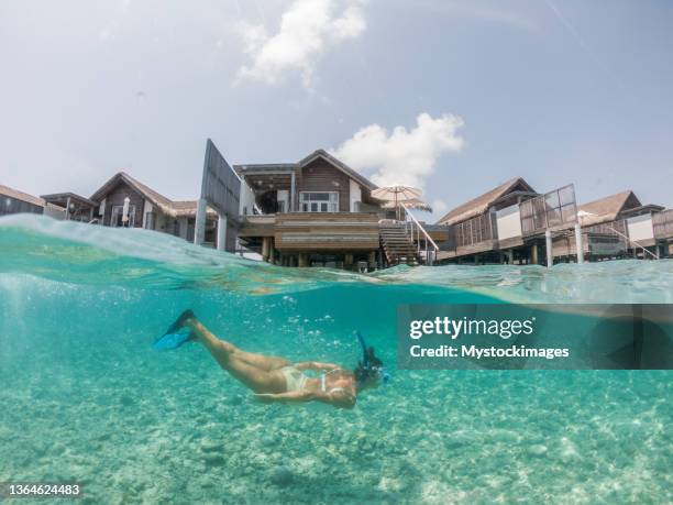 frau taucht im tropischen meer, split-screen-unterwasser-aufnahme, überwasser-villen auf demdat - schnorchel stock-fotos und bilder