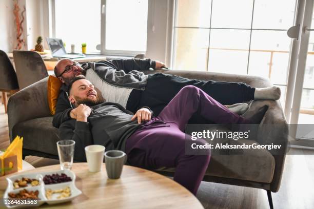 middle aged gay male and younger boyfriend relaxing on home sofa - male at home imagens e fotografias de stock