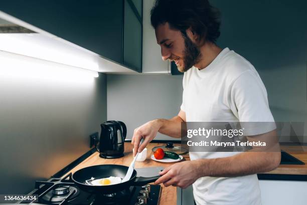 handsome guy is preparing scrambled eggs in the kitchen. fried eggs. modern cuisine. non-stick frying pan. man's hands. morning rituals. breakfast. - single life stock pictures, royalty-free photos & images