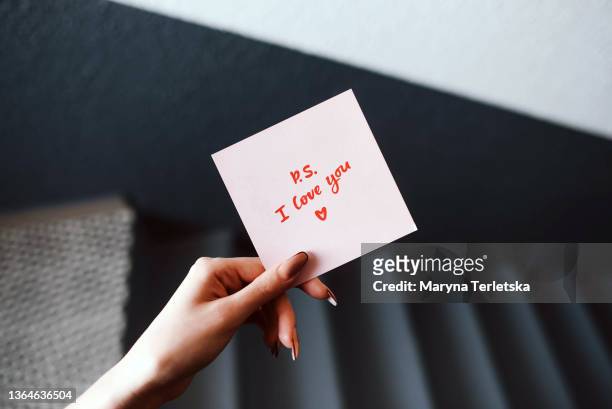 the girl holds in her hand a pink love note. valentine's day. gray background. woman's hand. declaration of love. love note. confession note. - love letter 個照片及圖片檔