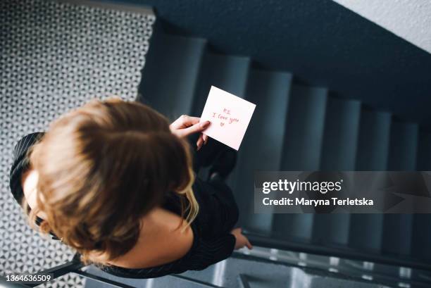 a girl stands on the staircase and reads a note. valentine's day. gray background. woman's hand. declaration of love. love note. confession note. girl with a note. the girl is reading. - love letter stock pictures, royalty-free photos & images