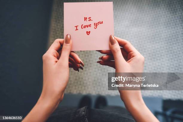 the girl holds a pink love note in her hands. valentine's day. gray background. woman's hand. declaration of love. love note. confession note. girl with a note. - hand holding stick stock pictures, royalty-free photos & images
