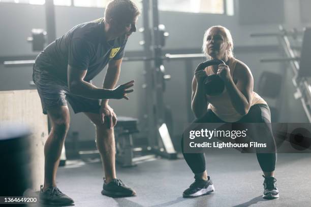 woman lifts kettlebell with personal trainer - personal trainer stock pictures, royalty-free photos & images