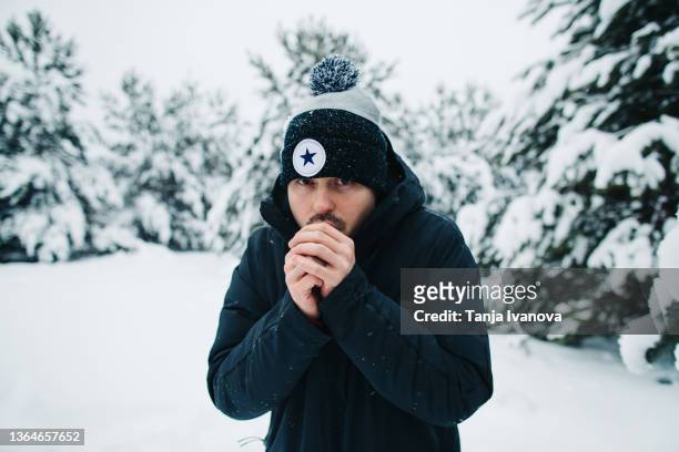 young man is frozen and warms his hands with his breath in the winter forest - bevriezing stockfoto's en -beelden