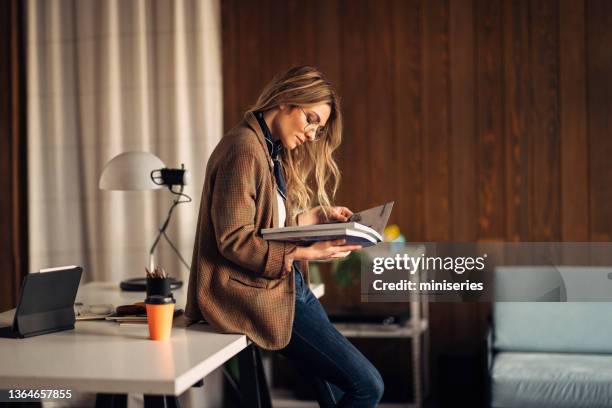 schöne geschäftsfrau sitzt auf ihrem schreibtisch und hält große bücher in der hand - catalogo stock-fotos und bilder