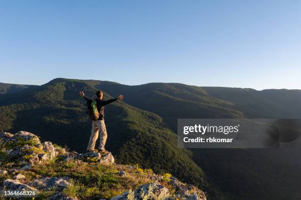 hiker cheering on rock in mountain scenery at sunrise - edge of cliff stock pictures, royalty-free photos & images