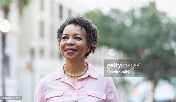 headshot of mature black woman walking on city street - pink shirt stock pictures, royalty-free photos & images