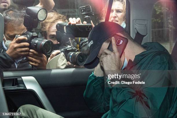 An unidentified man hides his face as members of the media photograph a car departing the offices of Serbian tennis player Novak Djokovic's legal...