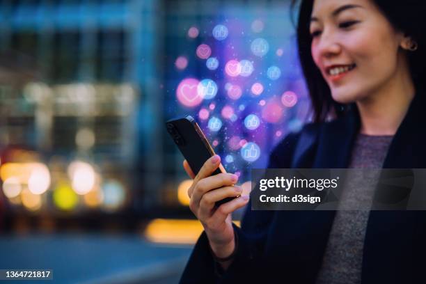 beautiful young asian woman using smartphone on social media network application on the go, viewing or giving likes, love, comment, friends and pages in the city at night. social media addiction concept - hong kong advertising stock pictures, royalty-free photos & images