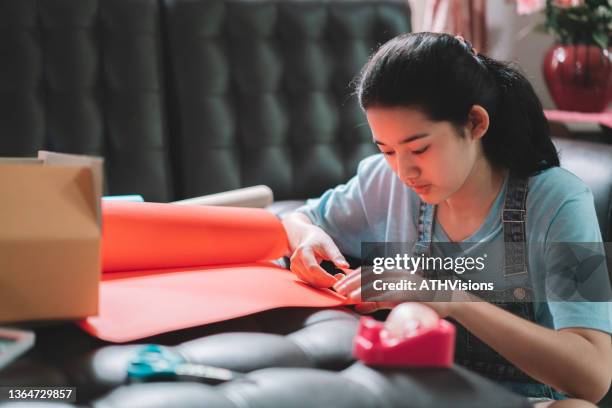 asian young teenager girl making handmade items care package by cutting a red paper prepare to sending to her family or friends from distance. - care package stock pictures, royalty-free photos & images