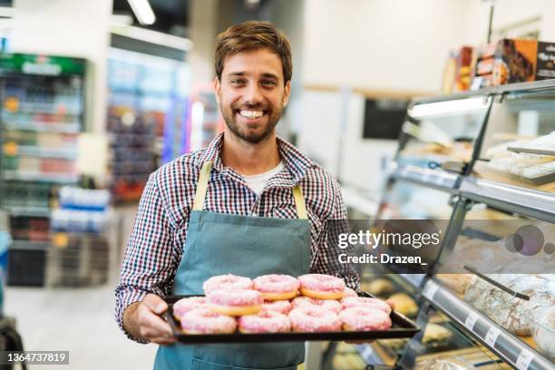 panadero en la tienda de comestibles sosteniendo donas y sonriendo a la cámara - buñuelo en forma de rosca fotografías e imágenes de stock