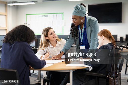 Female students working on assignment with help from teacher Female students working on assignment with help from teacher