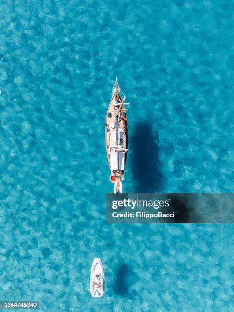 aerial view of a sailboat and a speedboat against a clear turquoise sea's water - blue sailboat stock pictures, royalty-free photos & images