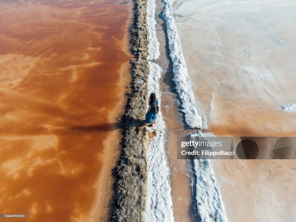 Aerial view of a woman standing in the middle of orange salt flats in Sicily, Italy