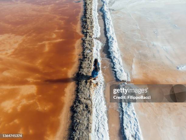 aerial view of a woman standing in the middle of orange salt flats in sicily, italy - marsala stock pictures, royalty-free photos & images