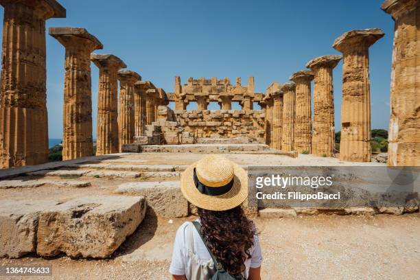 vista posteriore di una donna con un cappello mentre ammira un antico tempio in sicilia - turista foto e immagini stock