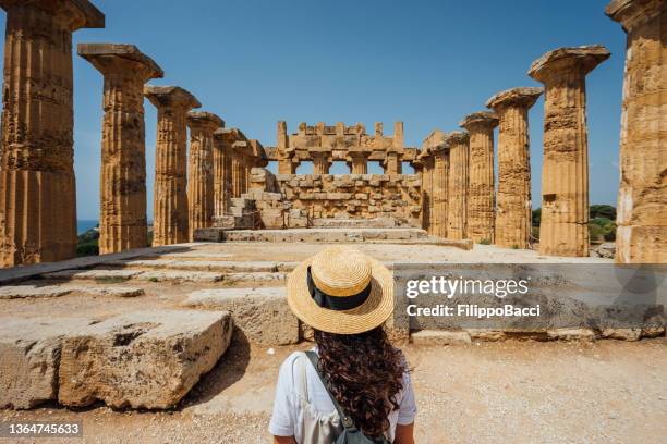 rear view of a woman with a hat while she's admiring an ancient temple in sicily - sociale geschiedenis stockfoto's en -beelden