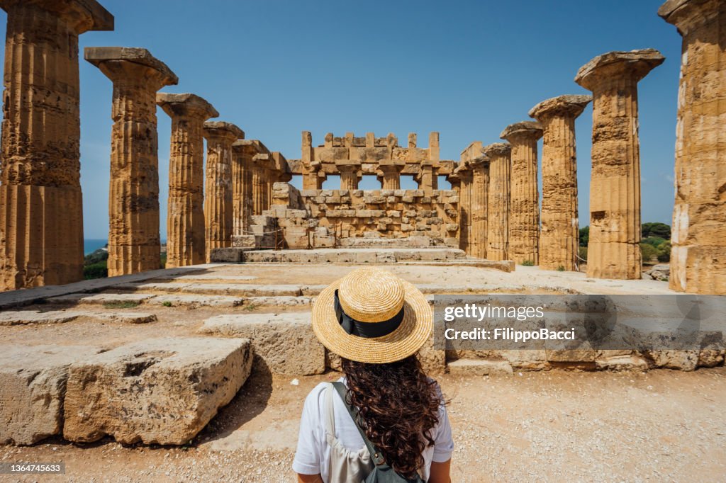 Rear view of a woman with a hat while she's admiring an ancient temple in Sicily