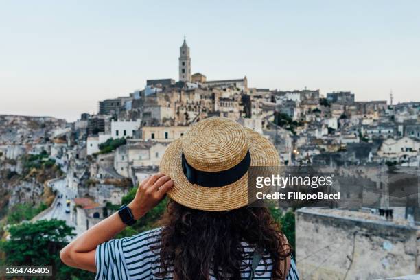 a woman with a straw hat is admiring the beautiful matera ancient city - matera stockfoto's en -beelden