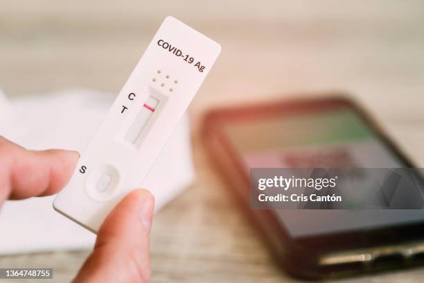 fingers holding a negative covid antigen test, covid certificate on phone and ffp2 mask in the background - equipo de autodiagnóstico fotografías e imágenes de stock