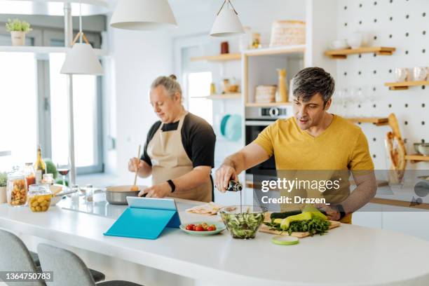 mature gay couple cooking lunch at home, using online tutorial - meal planning stock pictures, royalty-free photos & images