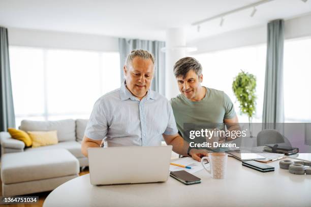 mature gay couple working from home - gay couple laptop stock pictures, royalty-free photos & images