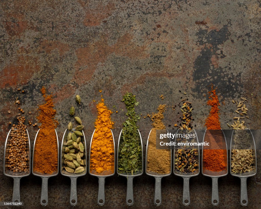 Muchas especias de comida india coloridas, orgánicas, secas y vibrantes en metal que miden cucharadas de alimentos secos sobre un viejo fondo de metal abstracto desgastado.
