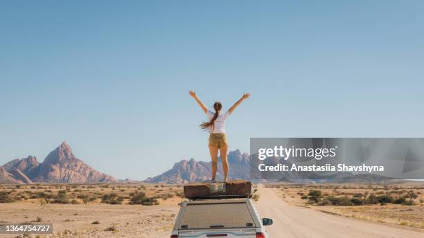 female traveler staying on top of the camper car enjoying the view of scenic landscape in namibia - arms raised mountain stock pictures, royalty-free photos & images