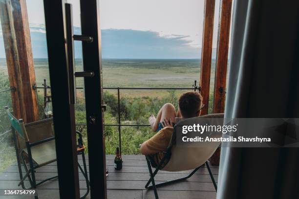 male traveler contemplating sunset at the wild savannah from the lodge terrace in etosha national park, namibia - balcony view stockfoto's en -beelden