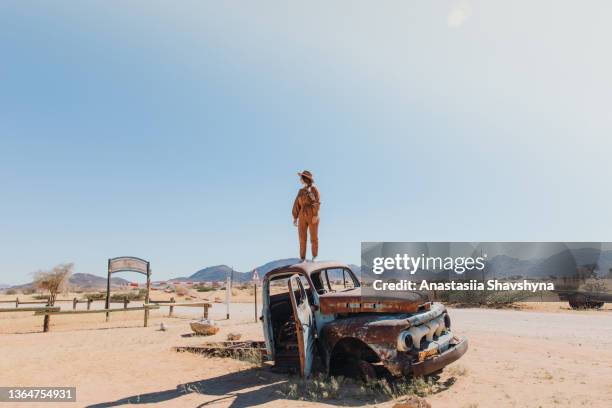 weibliche reisende mit hut sitzt im alten verlassenen auto mitten in der wüste in namibia - wildunfall stock-fotos und bilder