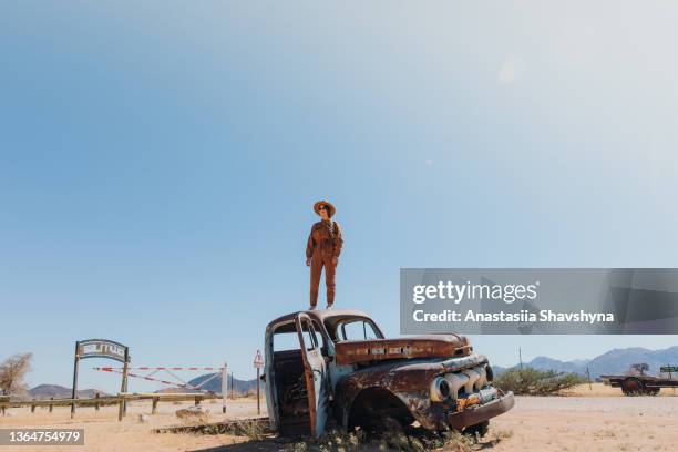 weibliche reisende mit hut sitzt im alten verlassenen auto mitten in der wüste in namibia - wildunfall stock-fotos und bilder