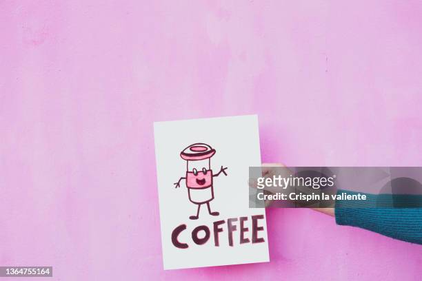 woman's hand holding a sign that says "coffee" on pink background - abrochar fotografías e imágenes de stock
