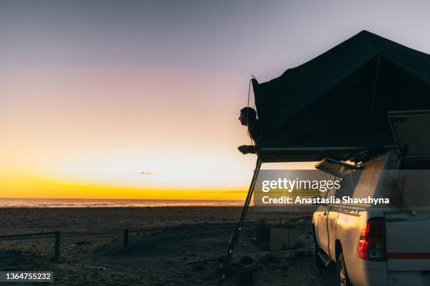 frau, die den malerischen sonnenuntergang am strand mit dachzelt camper car in namibia betrachtet - zelt stock-fotos und bilder