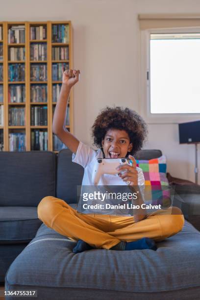 enthusiastic 10 year old boy raises his fist while playing video game console. - geballte faust stock-fotos und bilder