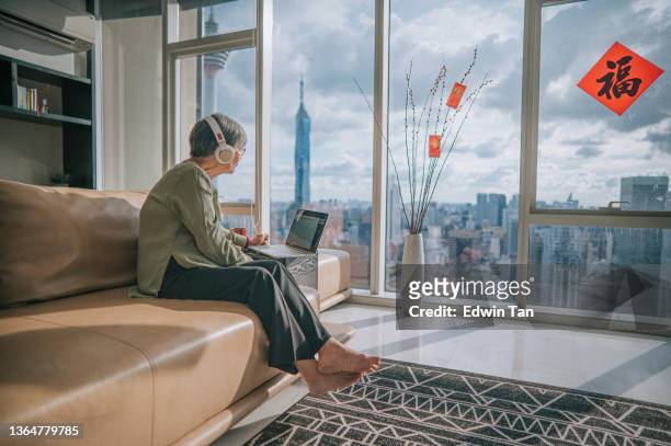 asian chinese senior woman using laptop video conference with her family members during chinese new year in living room of her apartment in city - 65 year old asian women stockfoto's en -beelden