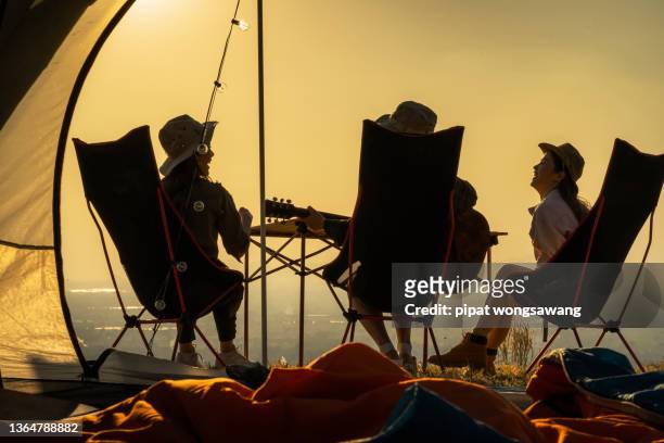 group of young asian friends playing guitar and singing in a tent during a summer camping vacation. concept of freedom, leisure, travel, adventure - camping friends stock pictures, royalty-free photos & images