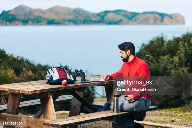 young hiker sitting with his open laptop on a camping ground with the bay of pollensa on the north coast of mallorca in the background - argentinien island stock pictures, royalty-free photos & images