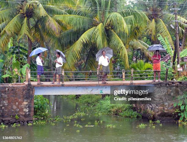 hombres de pie en un puente de vías fluviales bajo la lluvia, cochin, kerala, india - kerala rain fotografías e imágenes de stock