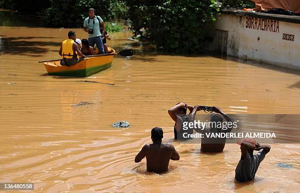 Local residents evacuate their homes on a boat and wading through a flooded street at the Tres Vendas neighborhood in Campos, 300 km north of Rio de...